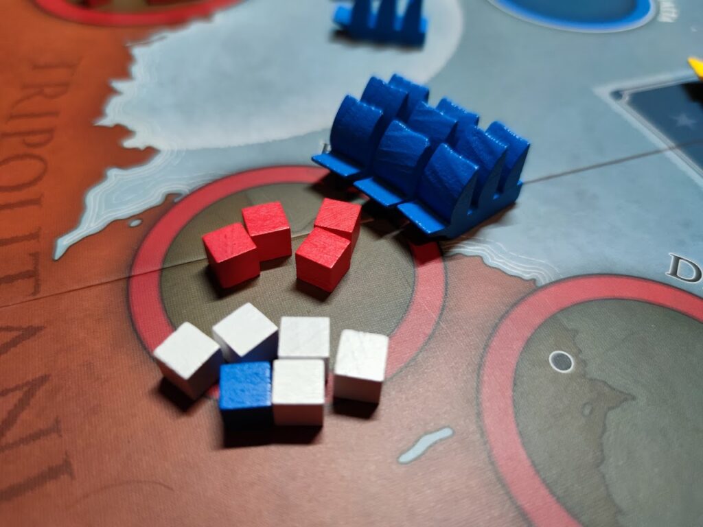 blue US frigates on the upper right of the picture are close to a harbour on the board. There are several red, blue and white cubes in the lower left of the image, which represent armies