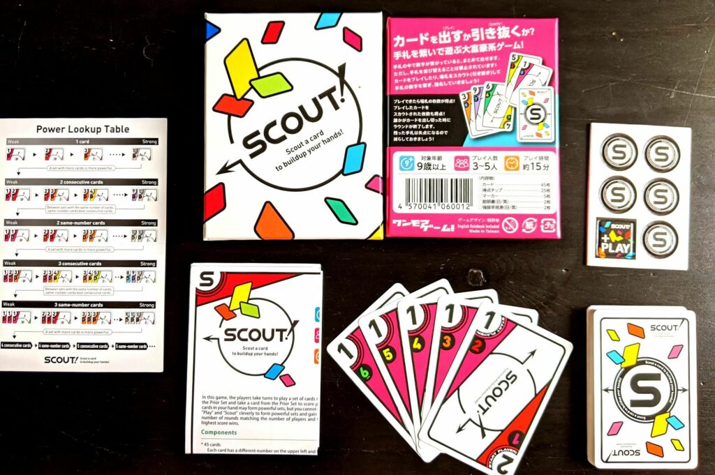 the original design of the Scout cards. Mostly white, with coloured edges. the cards and the box are displayed on a black table