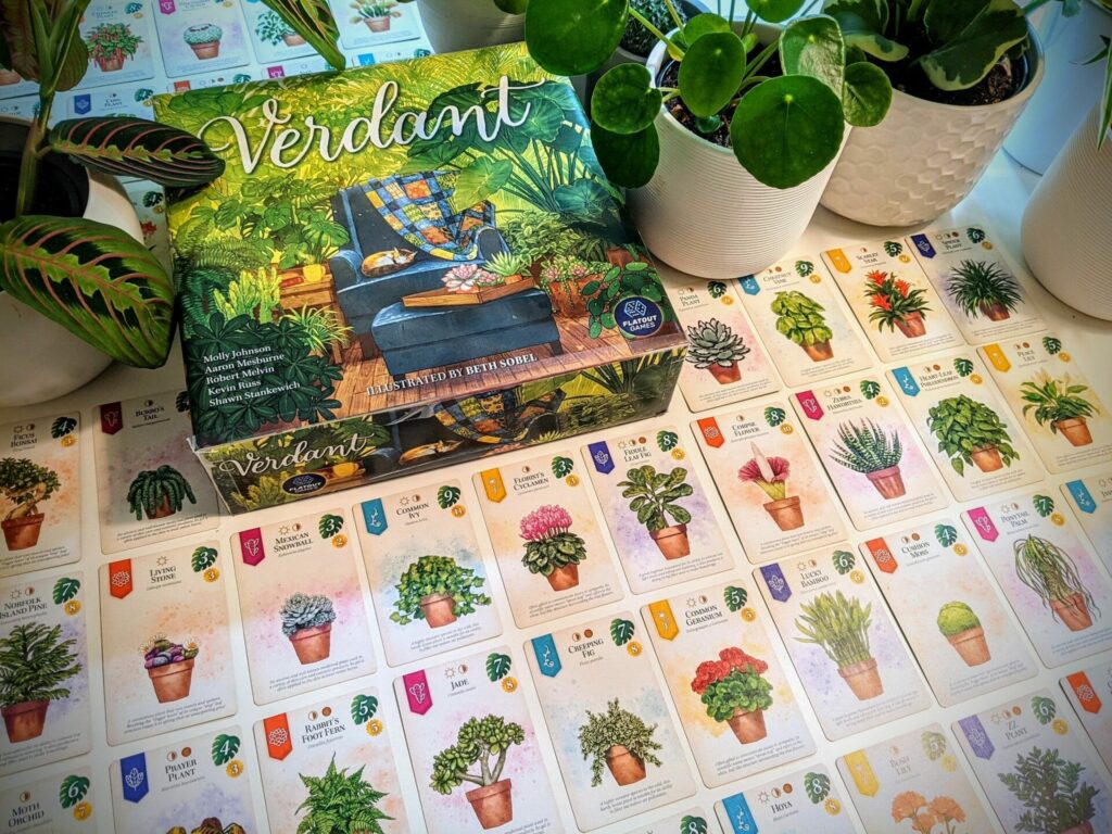 verdant game box contens The box and a lot of cards are spread on top of a table, with potted plants in the background