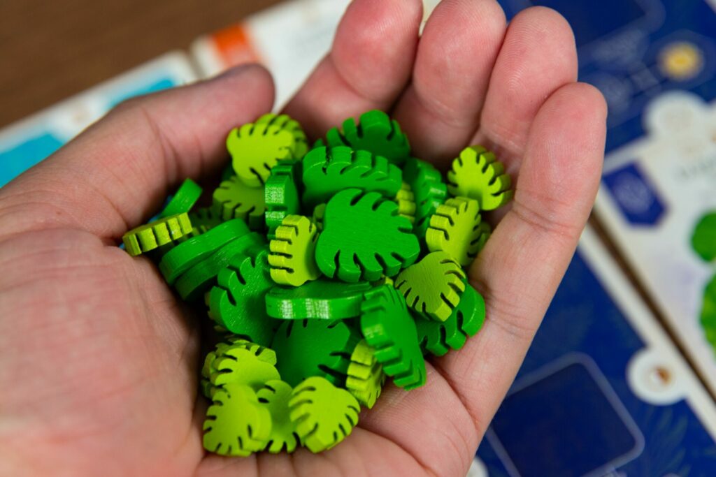 verdancy tokens from the verdant game. They are green, wooden, leaf-shaped pieces, held in a hand